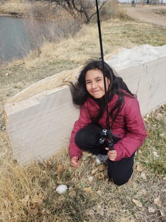 An AXL student with her fishing pole crouches near an egg on the ground during the field day fishing adventure.