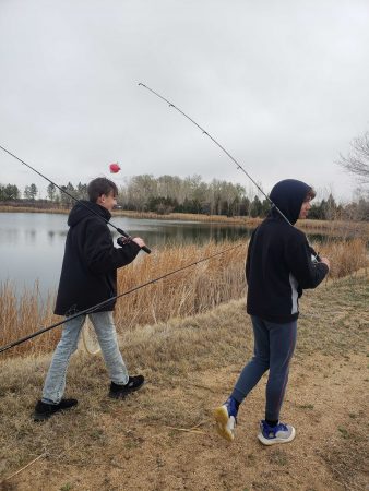 Two AXL students walk with fishing poles during their field day fishing adventure.