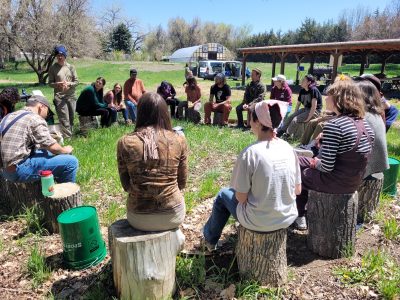 Attendees of the Ancestral Skills Gathering sit on logs in a circle at Ollin Farms.
