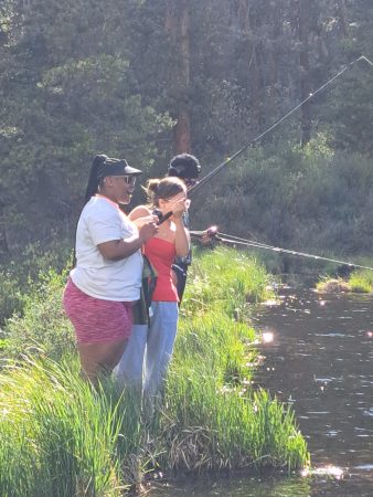 Three RiseUp students attempt to catch fish on a riverbank.