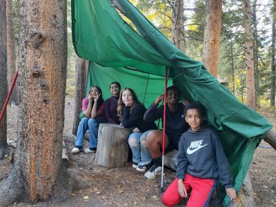 AXL students pose under their newly made tarp shelter during their first time camping trip.